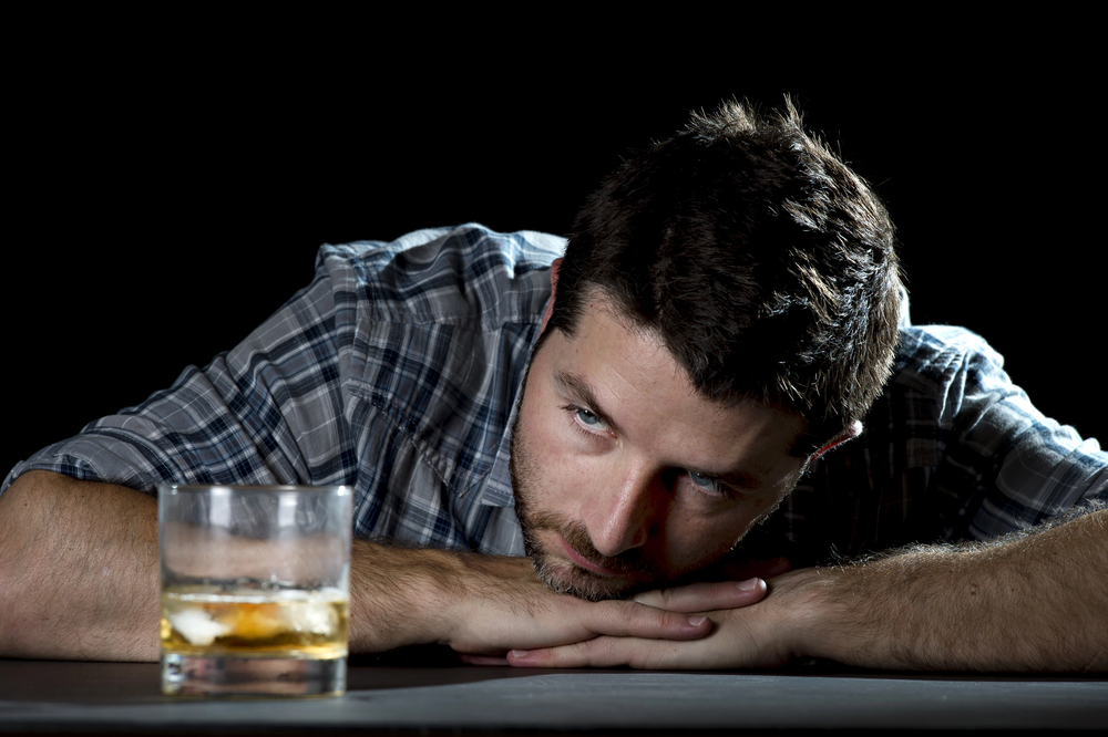 An alcoholic drunk man staring blankly into a glass of whiskey whose family is wondering how to commit someone to alcohol rehab